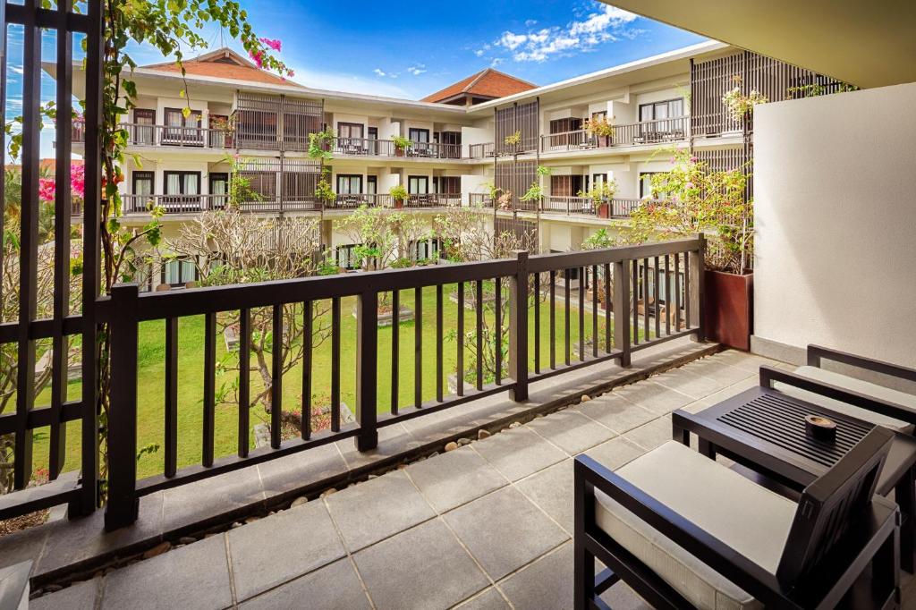 Balkons ar skatu uz dārzu, kas ieskauj viesnīcas ēku, ar ziediem un zaļām augiem. Mūsdienīgs mēbeļu komplekts papildina relaksējošo atmosfēru.