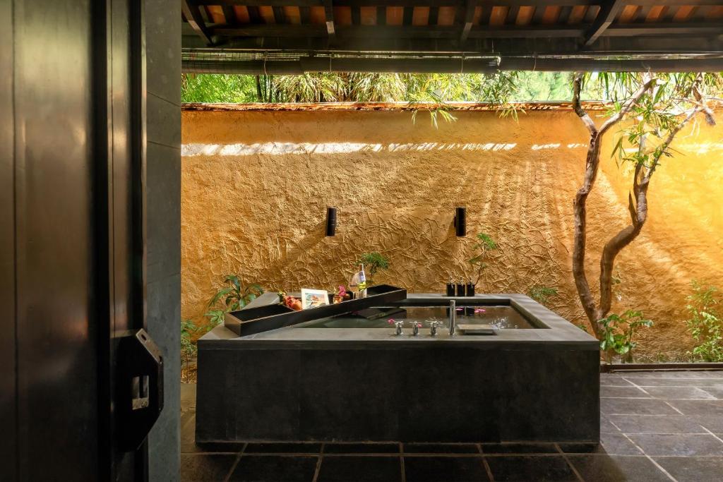 Mūsdienīgs un elegants vannas istabas interjers ar melnu akmens izlietni, kas atrodas tuvu dabai, ar zeltainu sienu un zaļumiem ap to. Ideāla vieta relaksācijai un atpūtai.