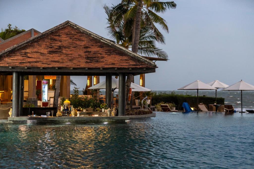 Eleganta pludmales vilnas, kas atspoguļo viesnīcas bāru ar modernu arhitektūru un baseinu, kas aicina uz atpūtu. Apkārt ir palmām un sauļošanās krēsliem, radot relaksējošu atmosfēru.