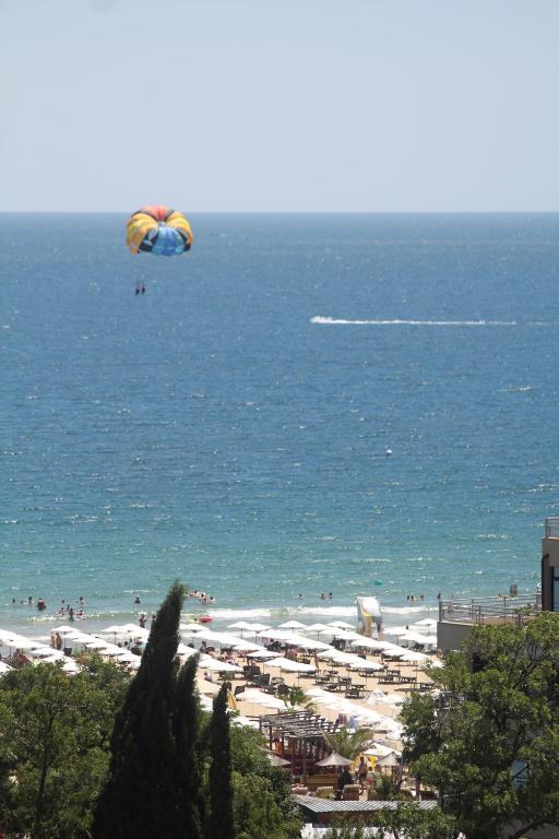 Paragliding virs jūras ar daudziem apmeklētājiem pludmalē. Skaista saulaina diena ar skaidru zilu ūdeni un pludmales krēslām.
