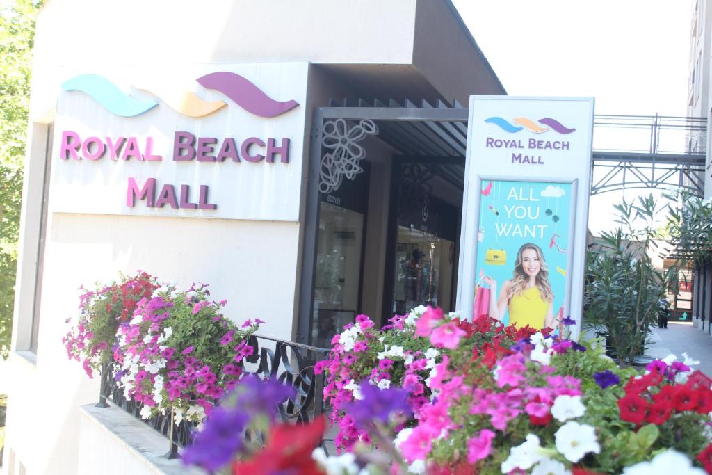 Royal Beach Mall ieeja ar krāsainām puķēm un reklāmas stendu, kas aicina apmeklētājus izbaudīt iepirkšanās pieredzi.