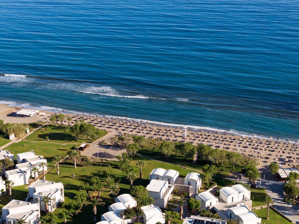 Pludmales ainava ar zilo jūru, smiltīm un saulessargiem, apzaļumota teritorija un viesnīcu komplekss.