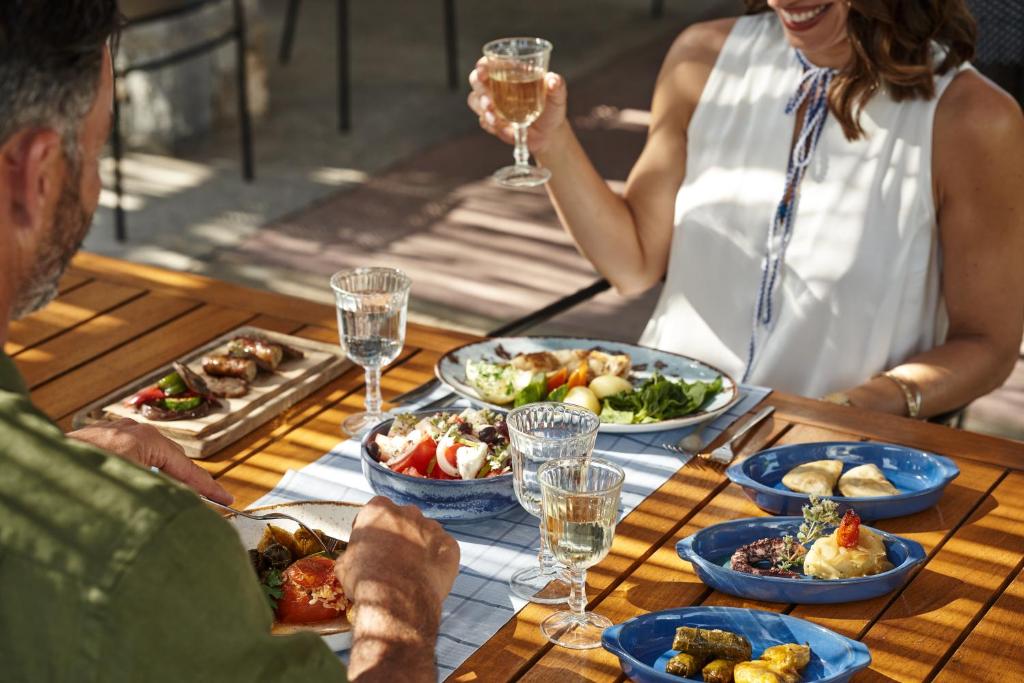 Skaista maltīte uz terases, kurā redzami dažādi ēdieni, piemēram, salāti, dārzeņi un gaļas ēdieni, kopā ar dzērieniem un cilvēkiem, kas priecājas par kopīgu laiku.