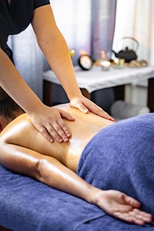 Masāžas sesija, kurā profesionāls masieris veic relaksējošu masāžu uz klienta muguras ar eļļu. Fons ar sveču gaismu un relaksējošu atmosfēru.