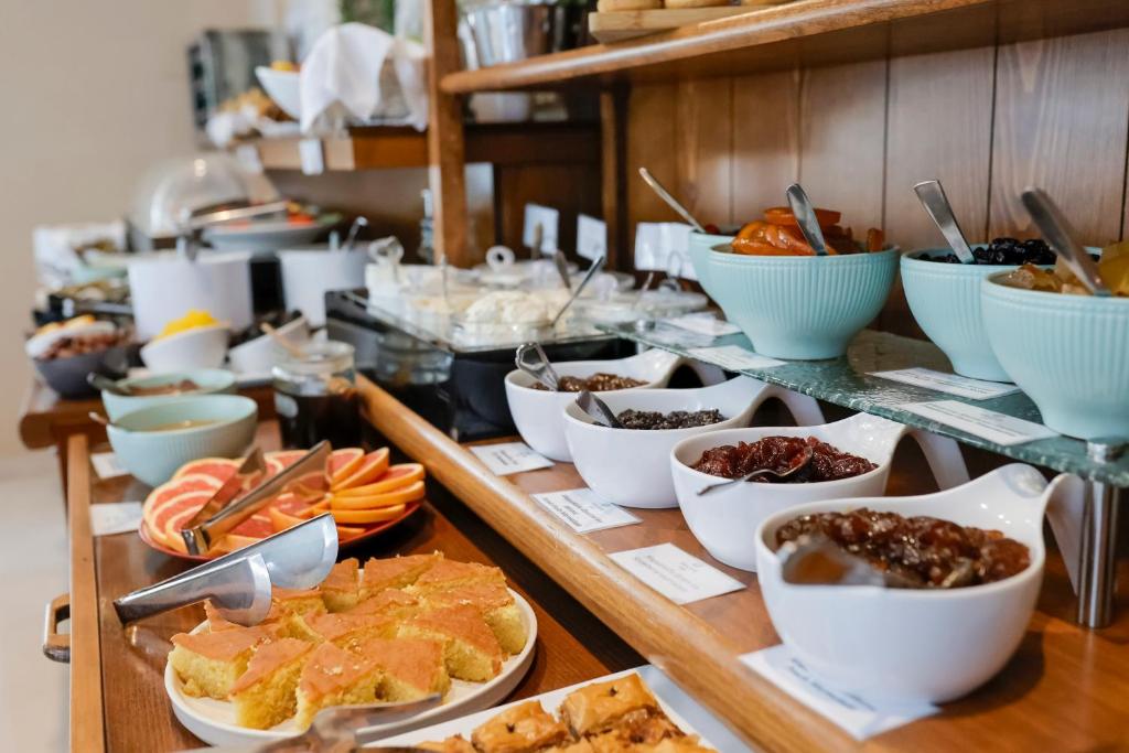 Broka, kas piedāvā dažādus augļus, saldumus un desertus, izvietota uz koka plaukta. Galda un apkalpošanas piederumi sakārtoti kārtīgi, radot viesmīlīgu atmosfēru.