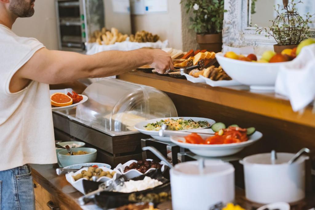 Vīrietis ņem ēdienu no bufetes, izvēloties no dažādiem dārzeņiem, augļiem un maizes. Uz galda ir arī saldumi un citi gardumi.