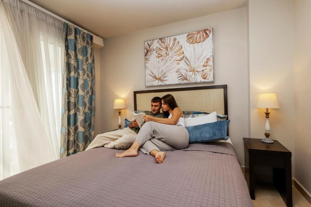 Jaunais pāris relaksējas gultā, lasot kopā grāmatu, apkārt ir mājīga istaba ar modernu interjeru un siltu apgaismojumu.