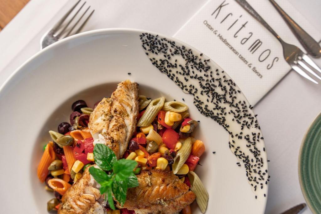 Svaiga zivs porcija ar dārzeņu un makaronu salātiem, rotāta ar melnajiem sezama sēklām, uz galda ar ēdienkarti restorānā Kritamos.