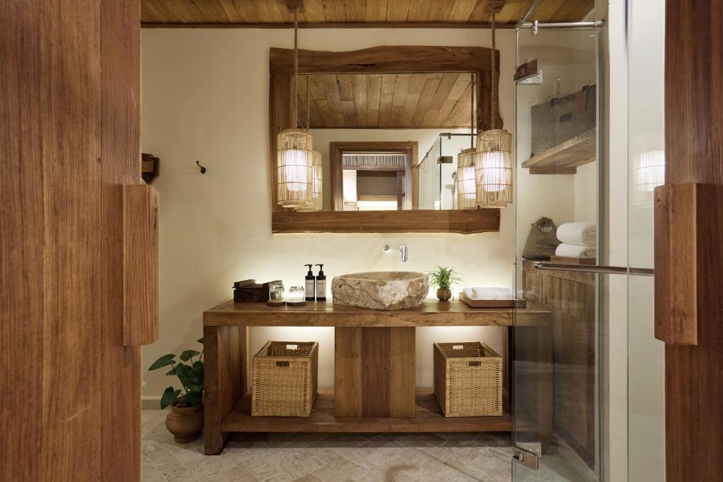 Mūsdienīgs vannas istabas interjers ar koka akcentiem, dabīgu akmeni izlietnē un siltu apgaismojumu. Telpa ir eleganta un harmoniska, radot relaksējošu atmosfēru.