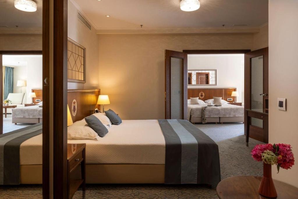 Elegants viesnīcas numurs ar divām guļamistabām, kurā redzams ērts gultas komplekts un mūsdienīgs interjers. Telpā ir gaismas un ziedu kompozīcija, kas piešķir mājīgumu.