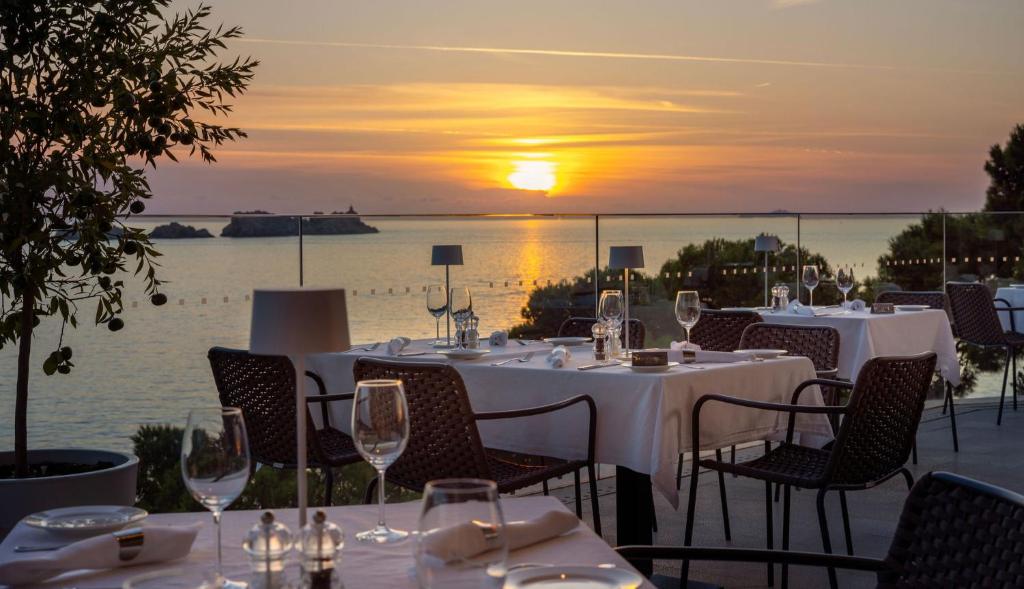 Romantiska vakariņu galdiņi ar skatu uz saulrietu pie jūras, apgaismoti ar mīkstu gaismu. Ideāla atmosfēra, lai izbaudītu brīnišķīgu maltīti.