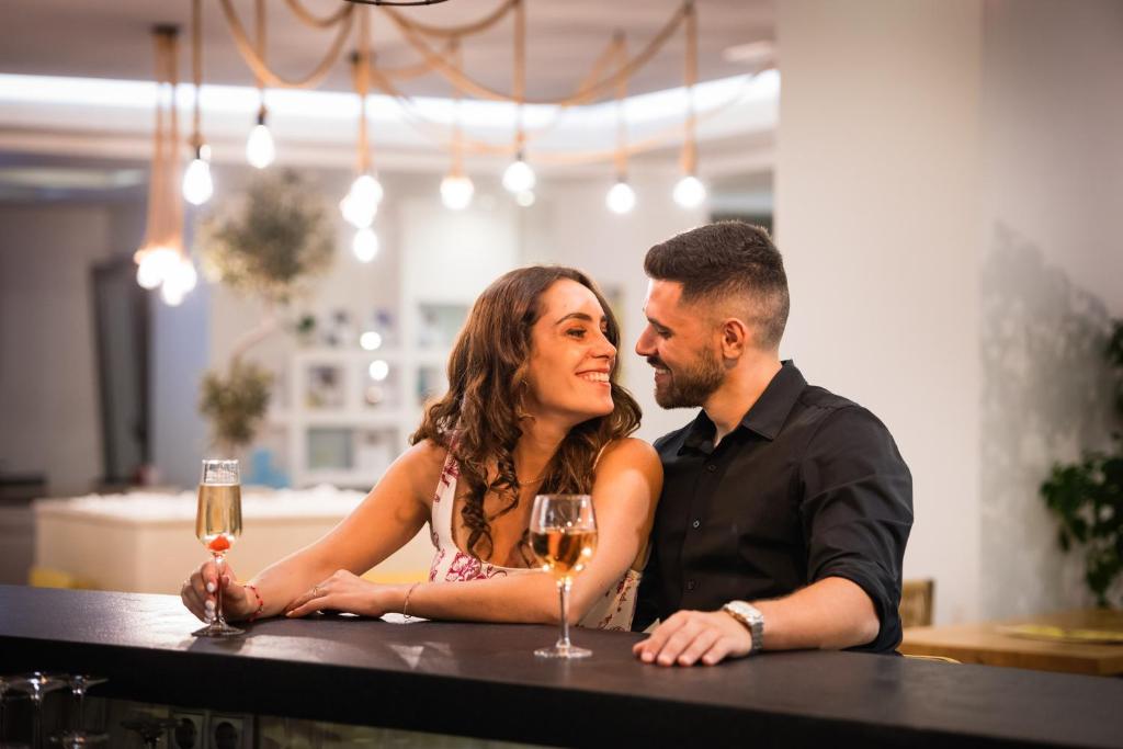 Jauna pāris sēž pie bāra, baudot dzērienus un skatoties viens otram acīs, radot romantisku atmosfēru. Apgaismojums ir maigs un mājīgs, veidojot intīmu vidi.