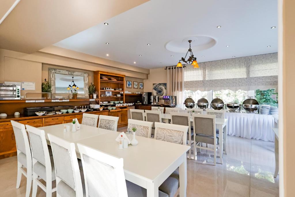 Gaiša un moderni iekārtota brokastu telpa ar baltām mēbelēm, bufetes galdu un daudzām ēdienu iespējām. Logi nodrošina dabīgu apgaismojumu un skatu uz dārzu.