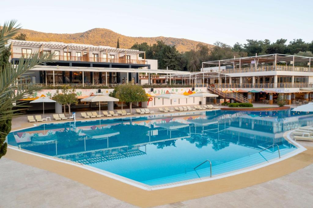 DoubleTree by Hilton Bodrum Isil Club Resort baseins ar saulessargiem un viesnīcu fonā
