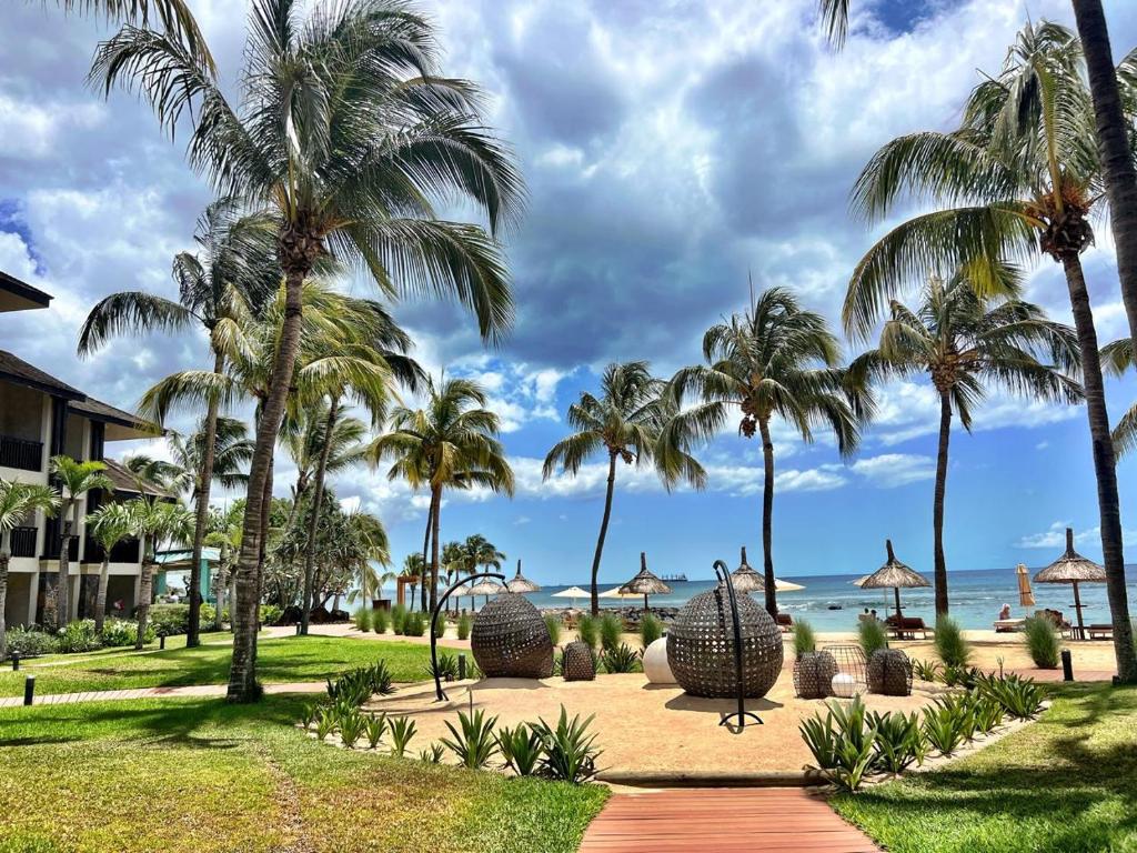 Tropiska pludmale ar palmām, zālienu un atpūtas laukumiem, kas vērsti uz jūru un saulainu debesu fonu. Ideāla vieta atpūtai un relaksācijai.