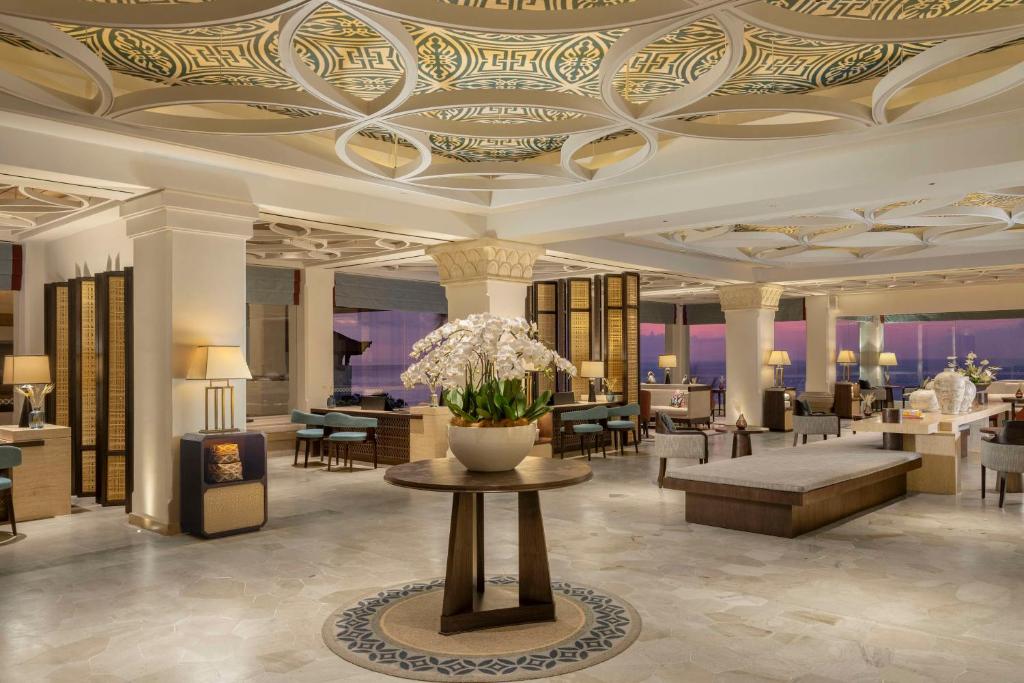 Elegantā viesnīcas uzgaidāmā telpa ar greznu griestu dizainu un ziedu kompozīciju centrā. Telpā ir mūsdienīgi mēbeļu komplekti un lielas logu ailes ar skatu uz dabu.