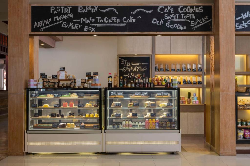 Konditorejas stends ar dažādiem kārumiem, tostarp kūkām, cepumiem un uzkodām. Virs vitrīnas ir izkārtojums ar informāciju par piedāvātajiem produktiem.