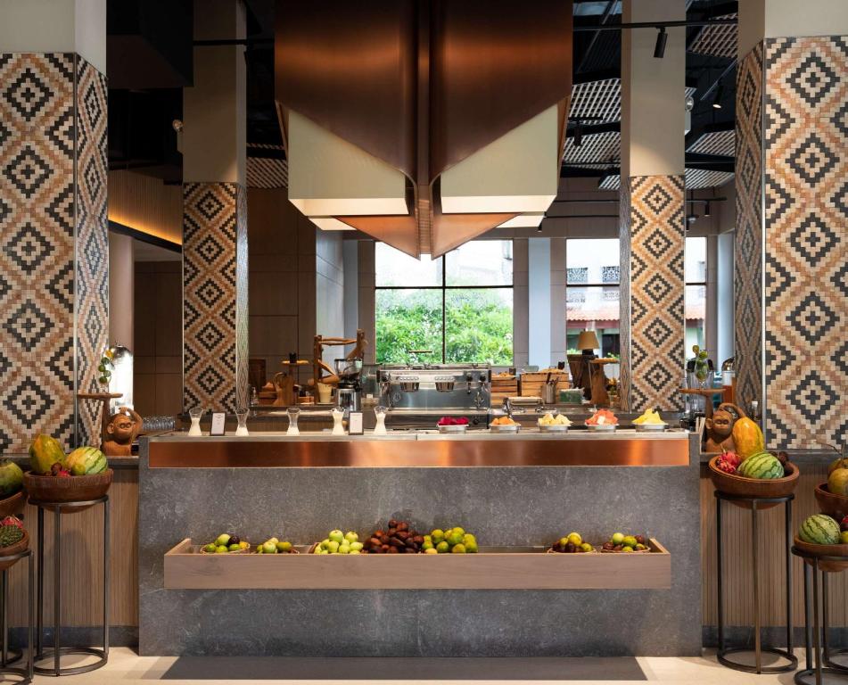 Mūsdienīgas restorāna virtuves interjers ar dekoratīviem flīzēm un augļu izkārtojumu uz galda, radot patīkamu un viesmīlīgu atmosfēru.