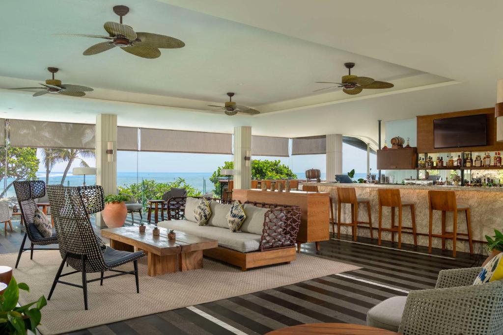 Mūsdienīgs un elegants viesnīcas bārs ar plašu skatu uz jūru, kurā ir komfortabli sēdvietas, koka galds un stilīgs interjers. Gaisma un dabīgā vide rada relaksējošu atmosfēru.