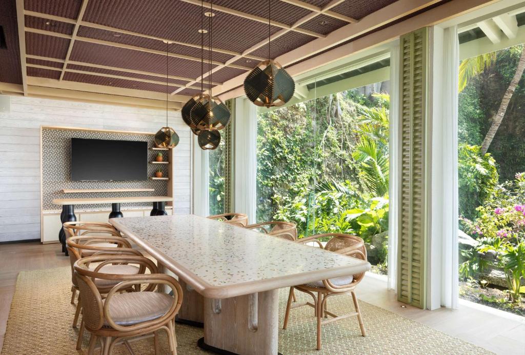 Grezns ēdamistabas interjers ar lielu galdu un ratiņiem, kas ieskauti zaļajā dārzā. Interjerā ir moderni apgaismojuma ķermeņi un televizors, kas papildina telpas dizainu.