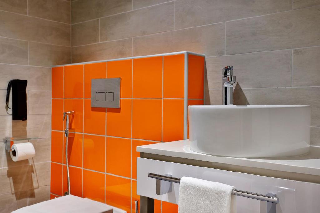 Mūsdienīga vannas istaba Aloft Al Mina viesnīcā ar spilgti oranžām flīzēm.