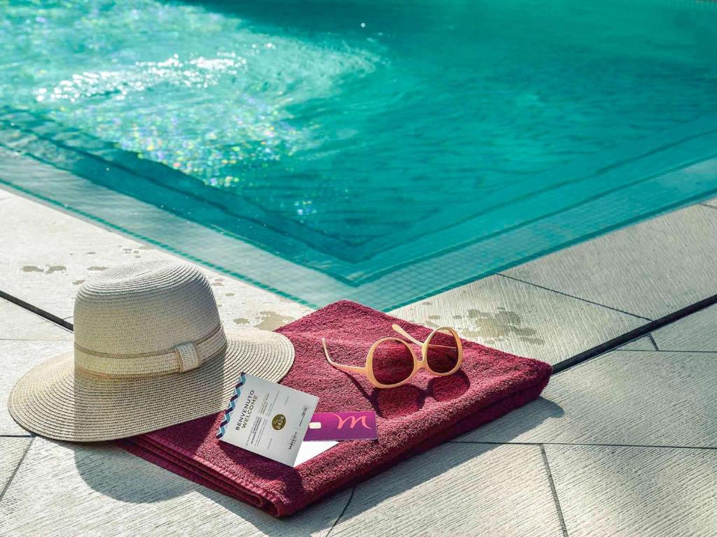 Saulaina pludmales atmosfēra ar peldēšanas basēna tuvumā novietotu dvieli, sauļošanās cepuri un saulesbrilles. Ideāla aina atpūtai un relaksācijai.