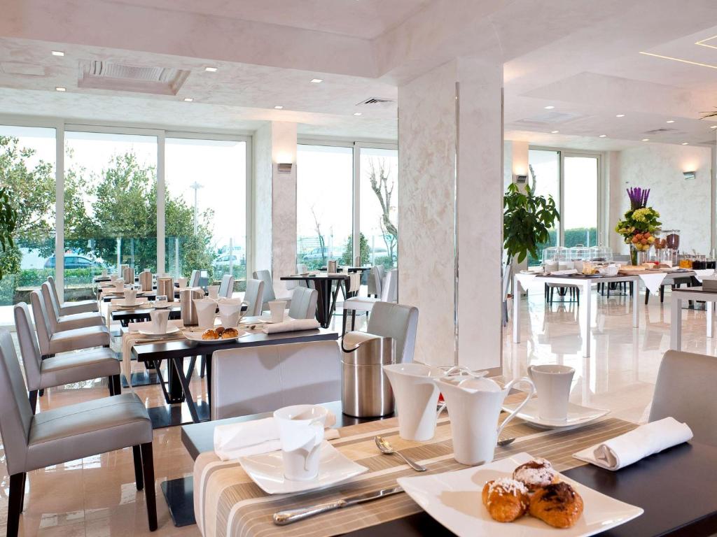 Mūsdienīgs restorāns ar gaišām telpām un skatu uz dabu, kur galdos ir novietoti kafijas un tējas trauki, kā arī gardas uzkodas. Interjers ir elegants un aicinošs, radot patīkamu atmosfēru.