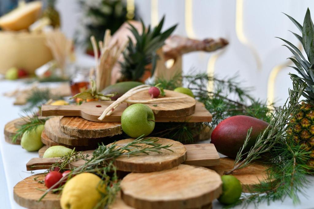 Dabīgā koka griešanas dēļi ar daudzveidīgiem augļiem, piemēram, āboliem, bumbieriem un ananāsiem, dekorēti ar zaļumiem, radot svinīgu un gardu atmosfēru.