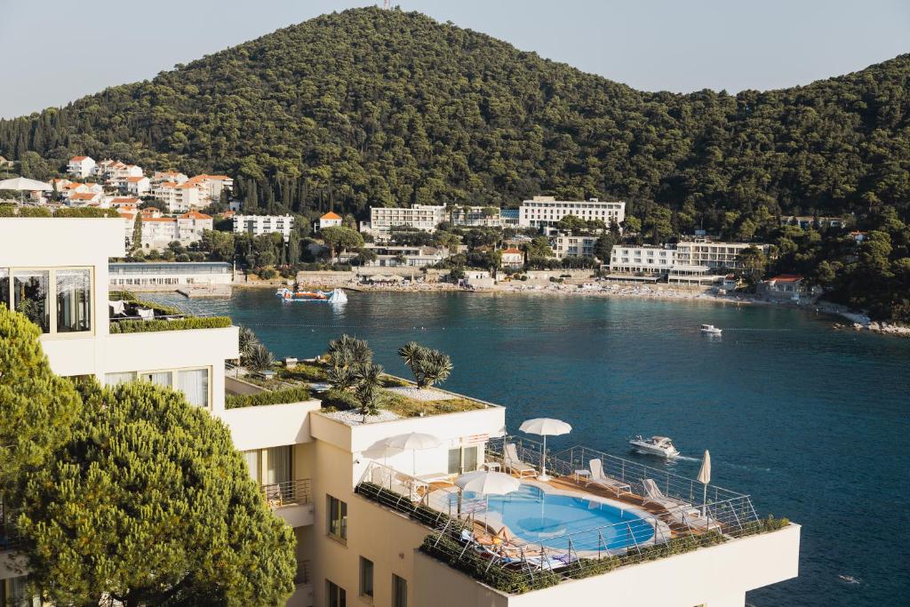 Mūsdienīga viesnīca ar baseinu uz jumta, kas atrodas pie gleznainas piekrastes, ar kalniem fona un apburošu skatu uz jūru.