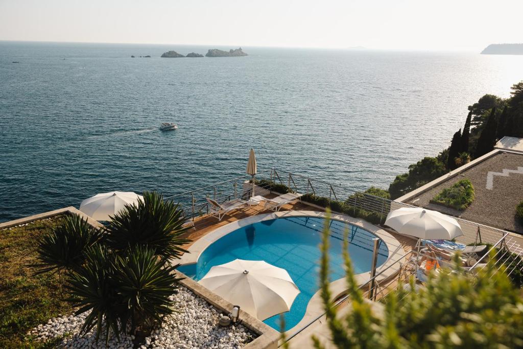 Peldbaseins ar skatu uz jūru un laivu, kas dodas pa ūdeni. Apkārt baseinam ir sauļošanās krēsli un lietussargi, radot relaksējošu atmosfēru.