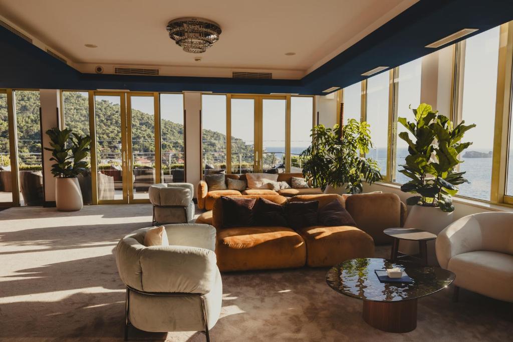 Mūsdienīgs un stilīgs viesistabas interjers ar plašiem logiem, kas piedāvā skatu uz dabu. Telpā ir ērti dīvāni, augi un eleganta kafijas galdiņa.