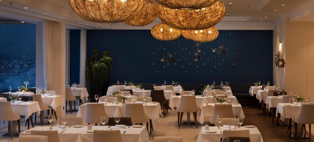 Elegants restorāns ar modernu interjeru, kurā ir baltas galdautu klātas galdi un stilīgas laternas. Gaisma rada patīkamu atmosfēru, ideālu romantiskām vakariņām.