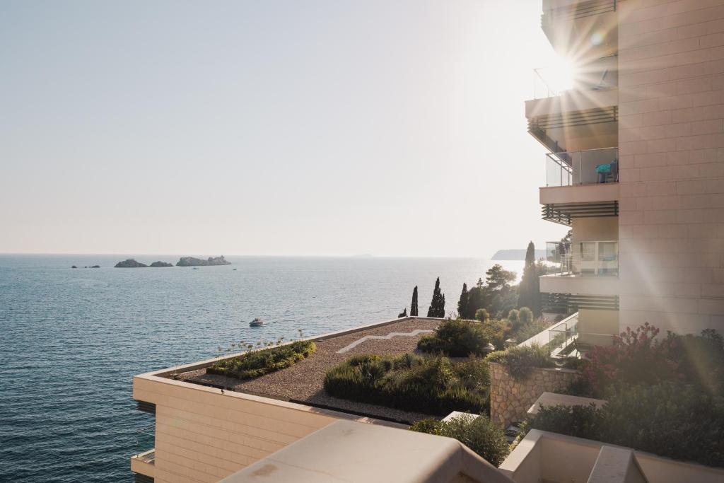 Skats uz jūru no modernas ēkas terases, ar saules stariem un zaļajiem augiem. Kluss un mierīgs ainava ar nelielām salām tālumā.