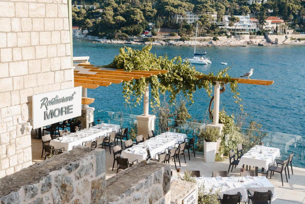 Restorāns ar nosaukumu "More" pie jūras, ar galdiem un krēsliem ārā, zaļumiem un skatu uz ūdeni. Ideāla vieta relaksācijai un ēdienreižu baudīšanai.