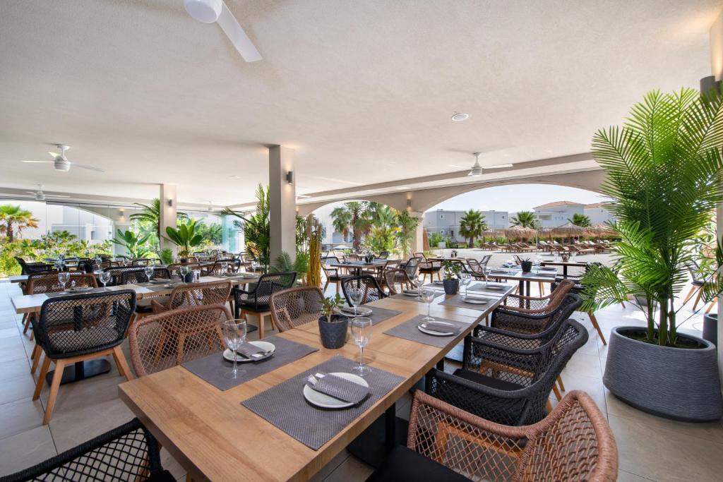 Mūsdienīgs restorāna interjers ar elegantiem galdiem un krēsliem, kas izvietoti zem jumta, ar zaļumiem un skatu uz baseinu. Ideāla vide relaksējošai maltītei.