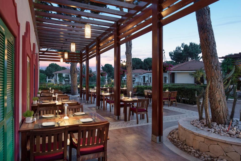 Ārējais restorāns pie viesnīcas Ela Excellence Resort Belek ar koka terasi un apgaismojumu.