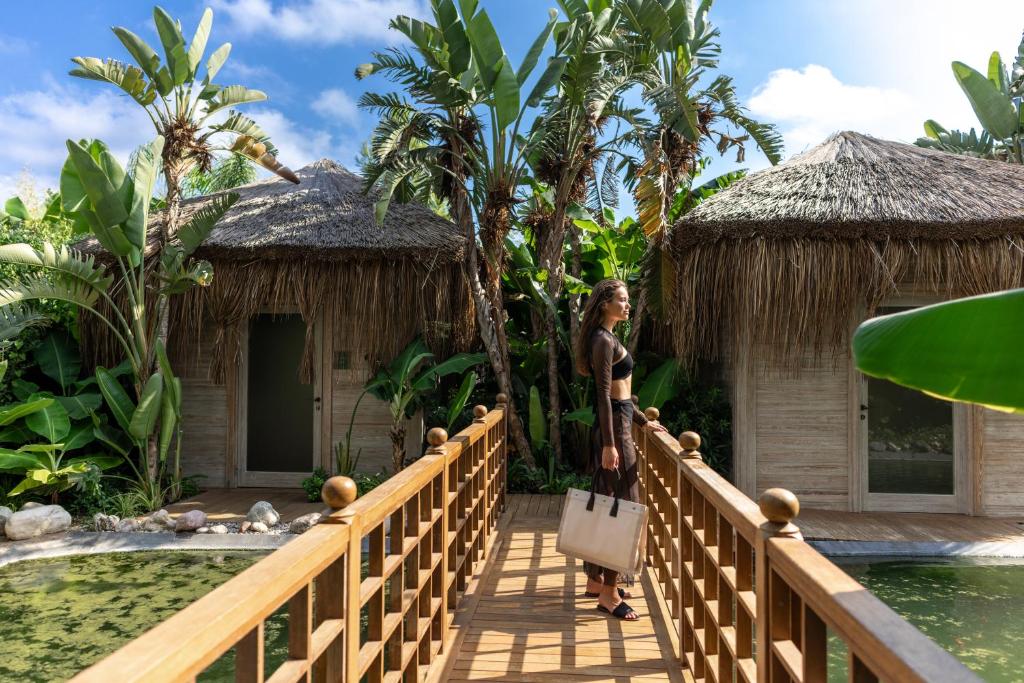Sieviete, kas staigā pa koka tiltu pie Ela Excellence Resort Belek, starp palmām.