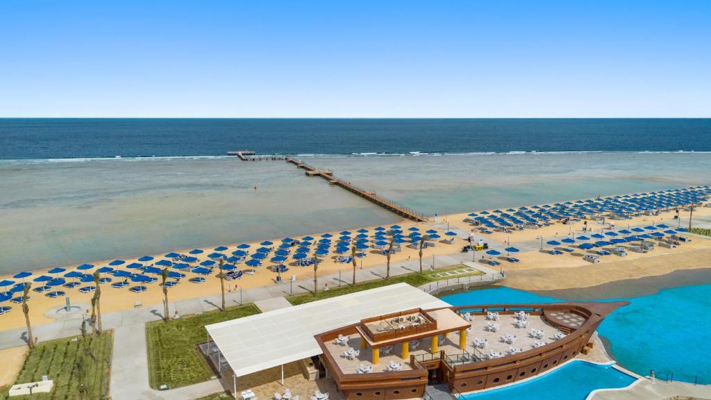 Pludmale ar saulessargiem un koka piestātni, kas vērsta uz mierīgu jūru, piedāvā relaksējošu atmosfēru. Redzams arī restorāns, kas veidots kā kuģis, pie piekrastes.