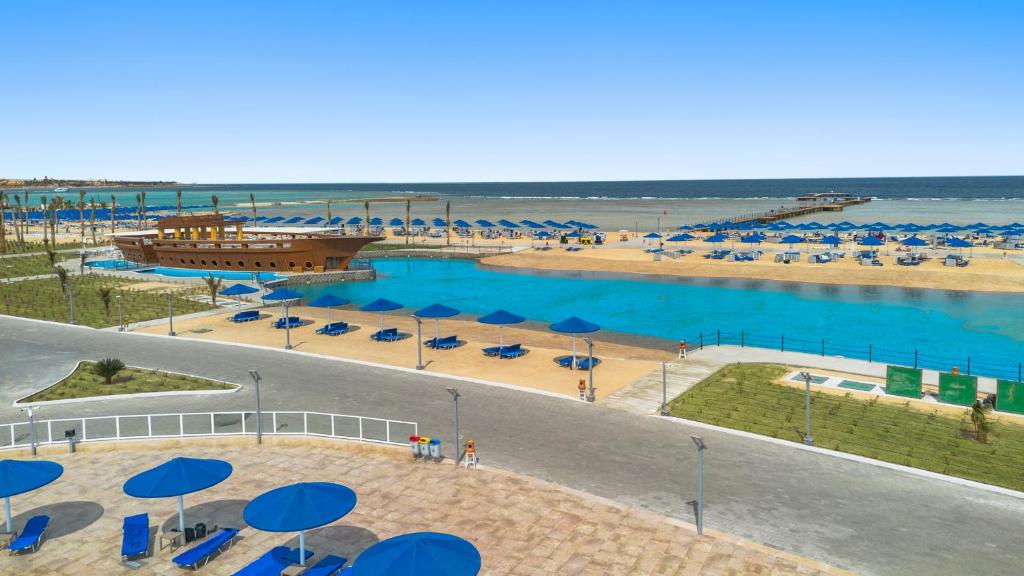 Pludmales ainava ar zilu ūdeni, smilšu pludmalēm un koka kuģi, kas atrodas tuvumā. Vairāki sauļošanās krēsli un saulessargi papildina relaksējošo atmosfēru.