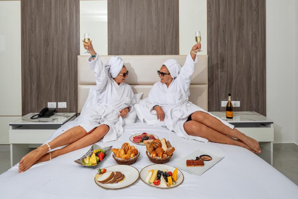 Divas sievietes baltajos halātus, turot šampanieti, atpūšas viesnīcas numurā, apņemot gultu ar dažādiem gardumiem un augļiem. Atmosfēra ir svinīga un relaksējoša.