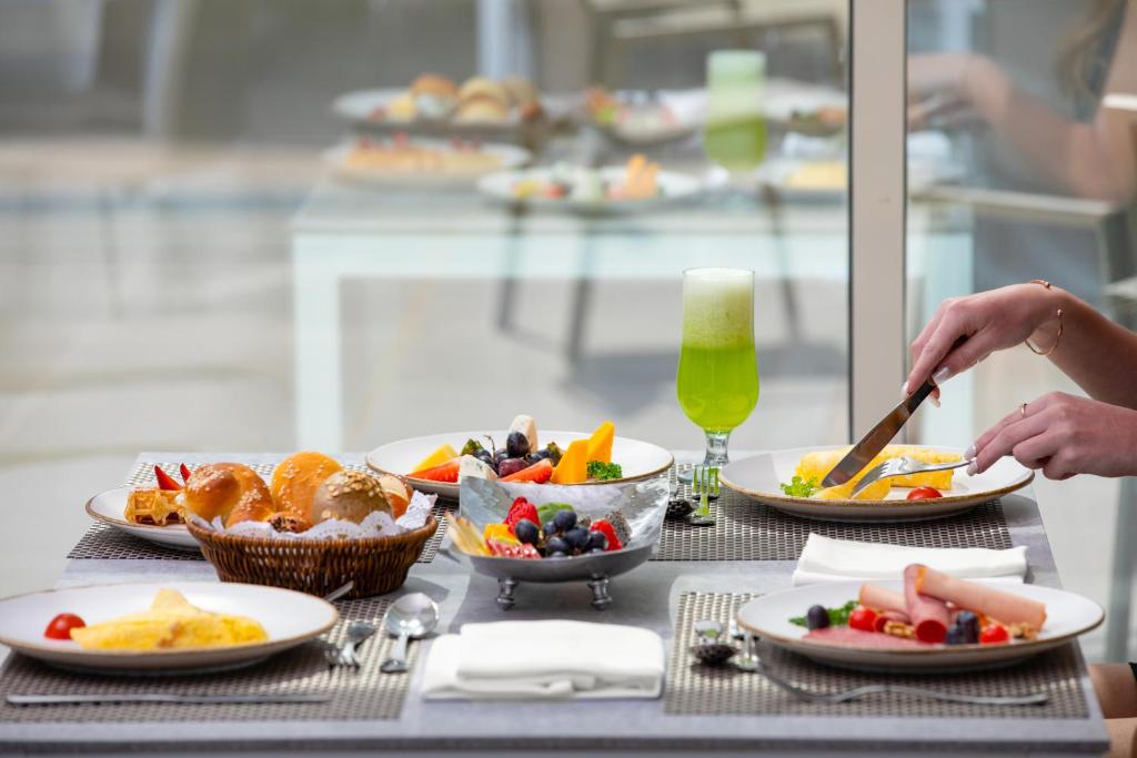 Brokastu galda ar dažādiem ēdieniem, tostarp maizēm, augļiem un zaļo dzērienu. Galda klāšana ir eleganta, radot patīkamu atmosfēru.