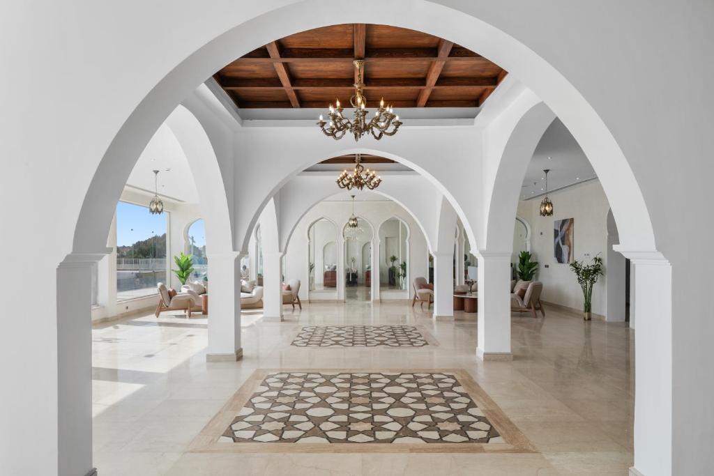 Mūsdienīgs interjers ar elegantām arched kolonnām un griestu lampām, kas izceļ gaišo un plašo telpu. Uz grīdas redzams dekoratīvs paklājs, bet logi piedāvā skatu uz dabu.