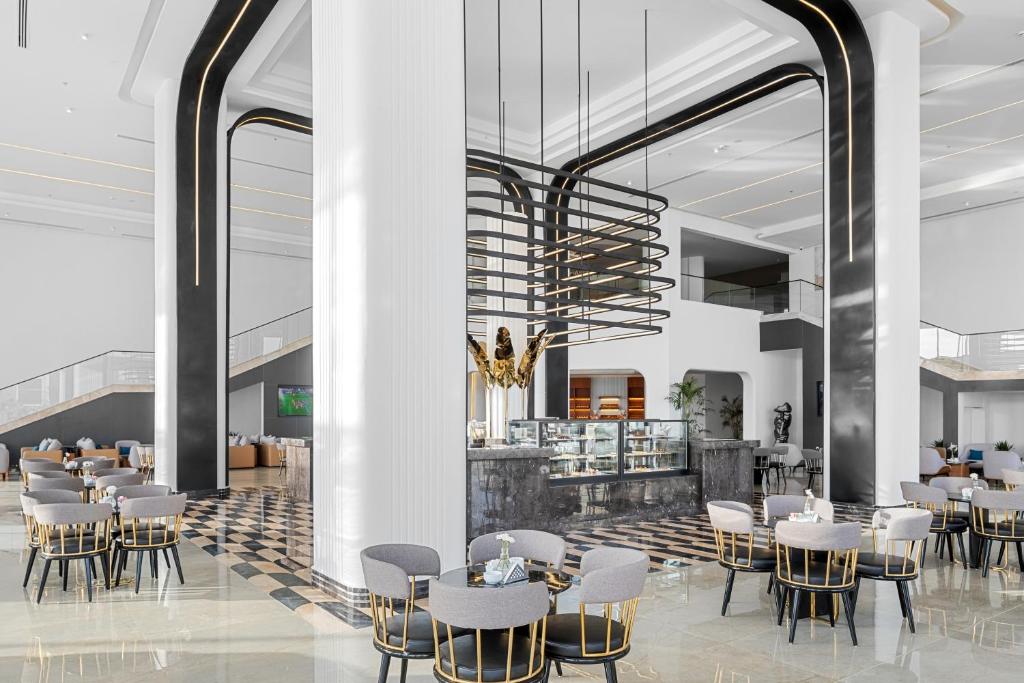 Mūsdienīga viesnīcas restorāna interjers ar elegantiem galdiem un krēsliem, centrā esoša izsmalcināta kafijas zona un stilīga gaismekļa konstrukcija. Gaismas un telpas harmonija rada patīkamu atmosfēru.