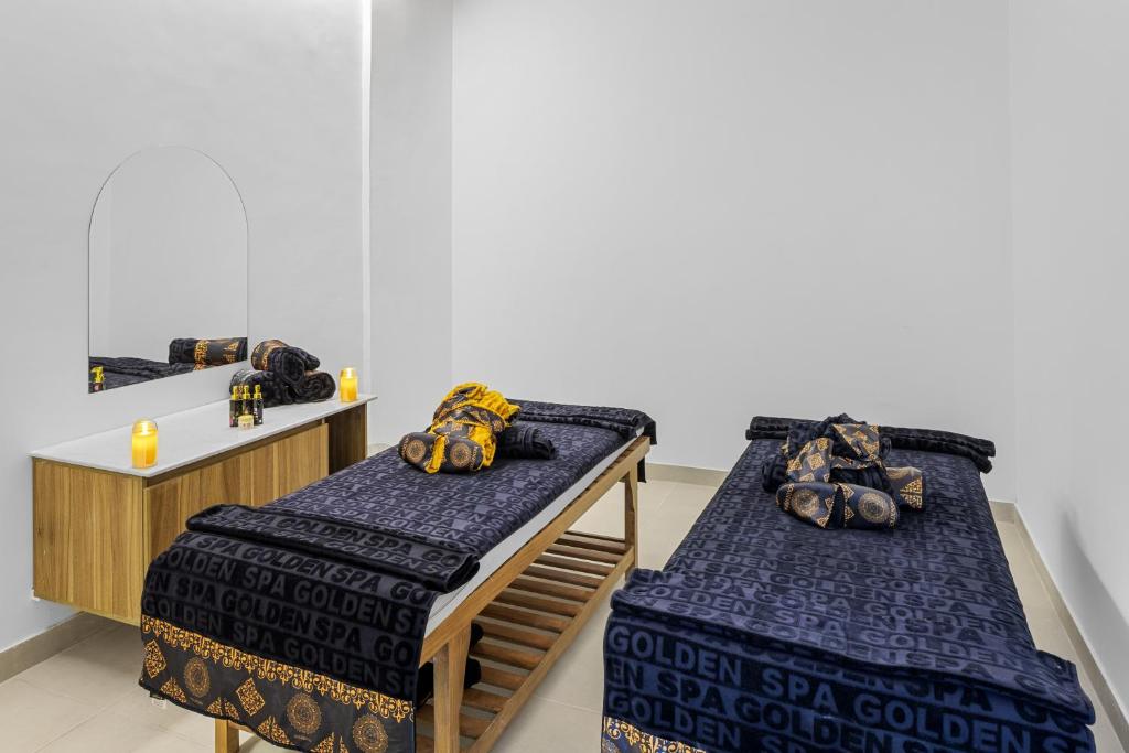 Relaksējoša spa telpa ar masāžas galdiem, dekorētiem ar melniem un zeltainiem dvieļiem. Uz galda novietoti aromātiskie sveces un eļļas, radot mierīgu atmosfēru.