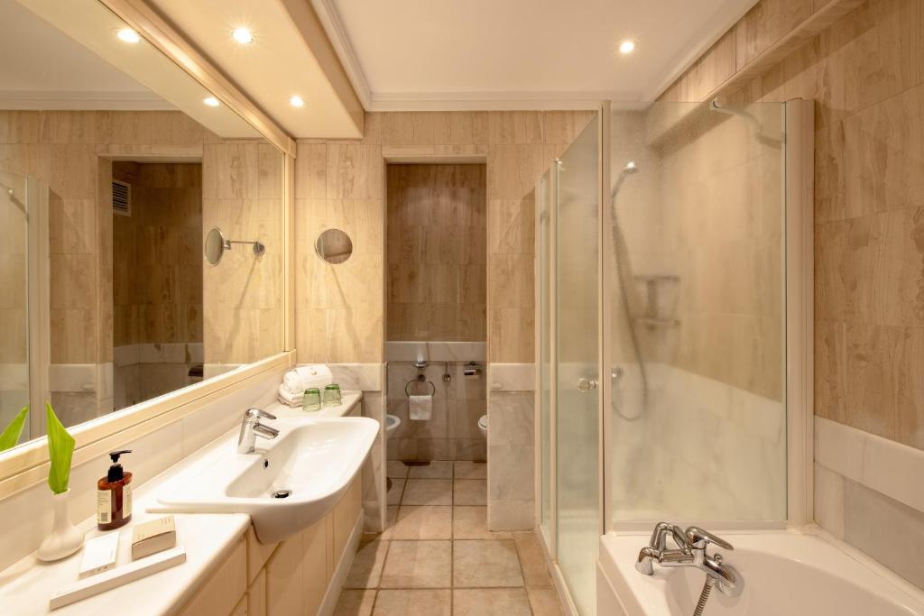 Mitsis Royal Mare viesnīcas vannas istaba ar mūsdienīgu dizainu un elegantu apgaismojumu.