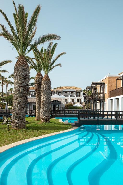 Mitsis Royal Mare baseins ar palmām un viesnīcas ēkām piekrastē