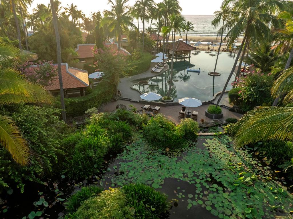 Tropu kūrorta ainava ar peldbaseinu, palmu kokiem un ziedošām krūmiem, kas atrodas blakus pludmalei. Dabas skaistums un relaksējoša atmosfēra.