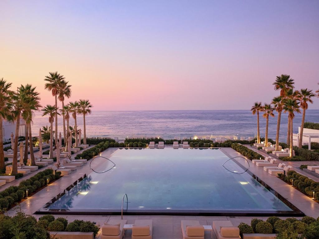 Grecotel Lux Me White Palace baseins ar skatu uz piekrasti saulrietā.