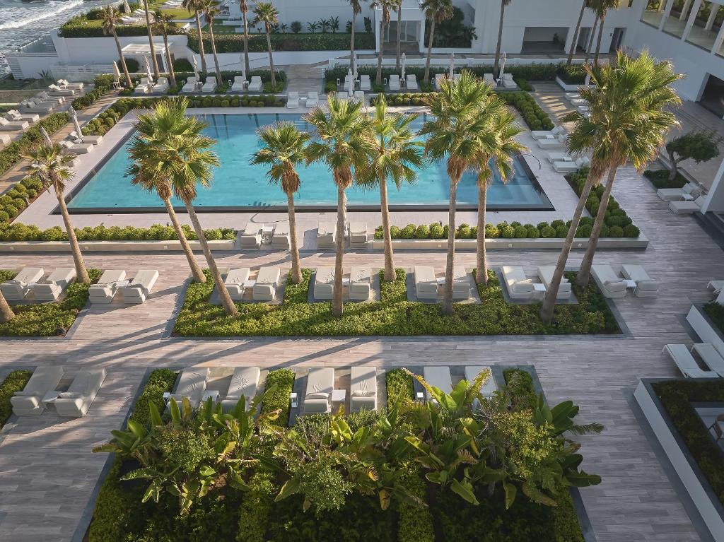 Grecotel Lux Me White Palace baseins ar palmām un atpūtas zonu piekrastē