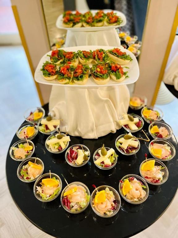 Eleganti izkārtoti uzkodu šķīvji ar salātiem un garnelēm, kas pasniegti stilīgā melnā plāksnē. Kārtainie salāti ar dārzeņiem un augļiem pievieno krāsainību svinībām.